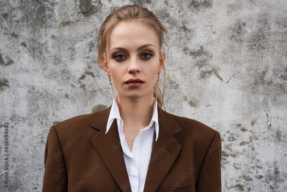 young woman in stylish brown blazer posing near concrete wall young woman in stylish brown blazer posing near concrete wall