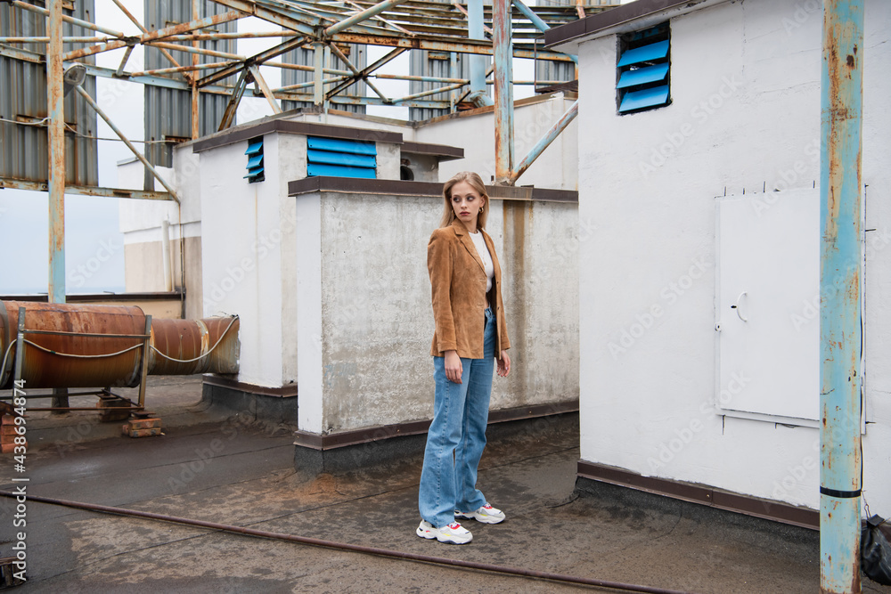 full length of pretty woman in stylish outfit with jeans and trendy sneakers standing on rooftop