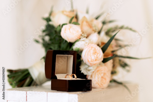 Wedding gold rings in a box next to a bouquet, on a light background.