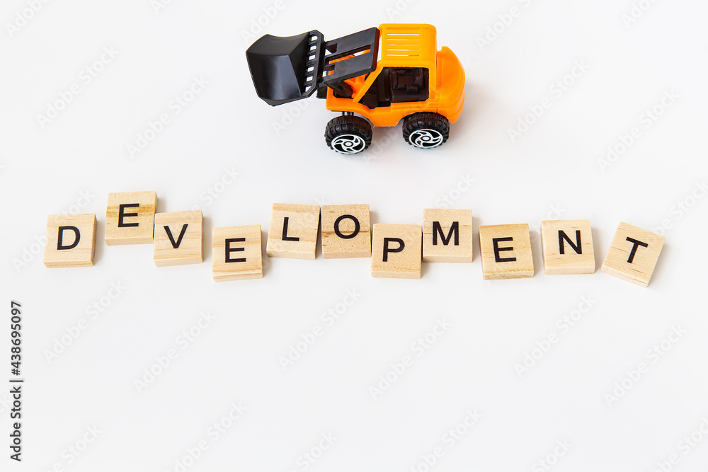 Development of the word written on a wooden block, development of the lettering, small toy tractor. The concept of line, renovation, development. Development of the word written on a wooden block, development of the lettering, small toy tractor. The concept of line, renovation, development.