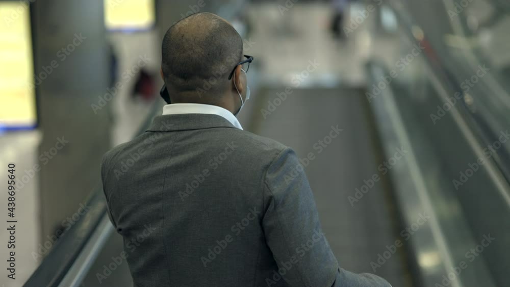 Young businessman with trolley bag talking on phone standing at escalator in the airport. Traveling during pandemic must be social distancing. He check in airport terminal. Young businessman with trolley bag talking on phone standing at escalator in the airport. Traveling during pandemic must be social distancing. He check in airport terminal.