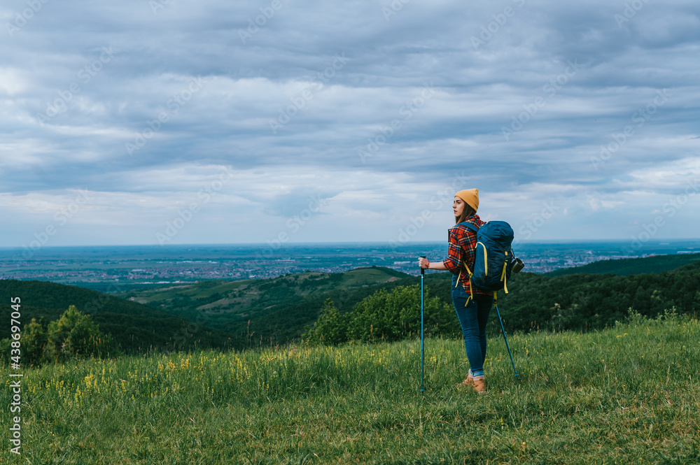 A young hiker woman using trekking poles and wearing backpack