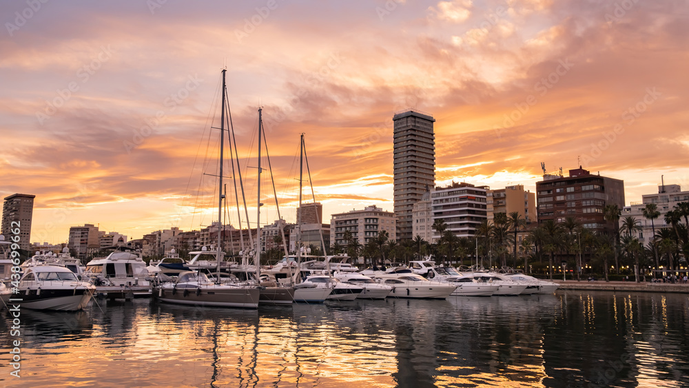 Alicante harbor with luxury yachts and sailboats, promenade palm trees in old town at sunset, Spain. Beautiful view of touristic town port in Costa Blanca region on Mediterranean sea coast.