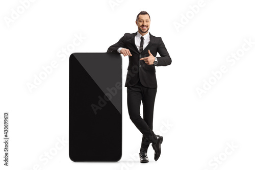 Full length portrait of a young professional man standing next to a big smartphone and pointing photo