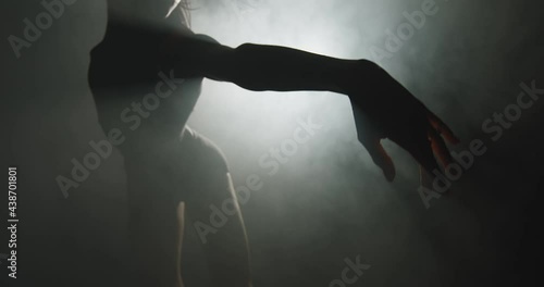 Modern ballet performance. Silhouette of graceful ballerina dancing mysterious dance in textured smoke in spotlight
