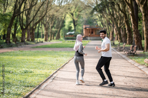 Happy arabian couple in active wear jogging at green park during morning time. Young man and woman enjoying time spending together. Common workout outdoors.