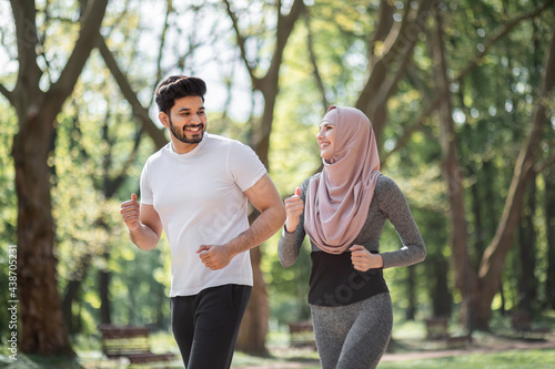 Healthy sport couple in active clothes enjoying morning run at green park. Muslim man and woman in hijab spending leisure time for training on fresh air.