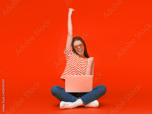 Foto She is a winner! Excited young female with laptop isolated on red background