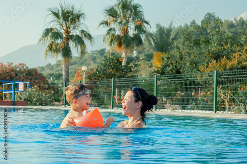 Mother and son in outdoor swimming pool. Kid learning to swim. Mom and child playing in water. Family summer vacation. Active and healthy sport for kids.