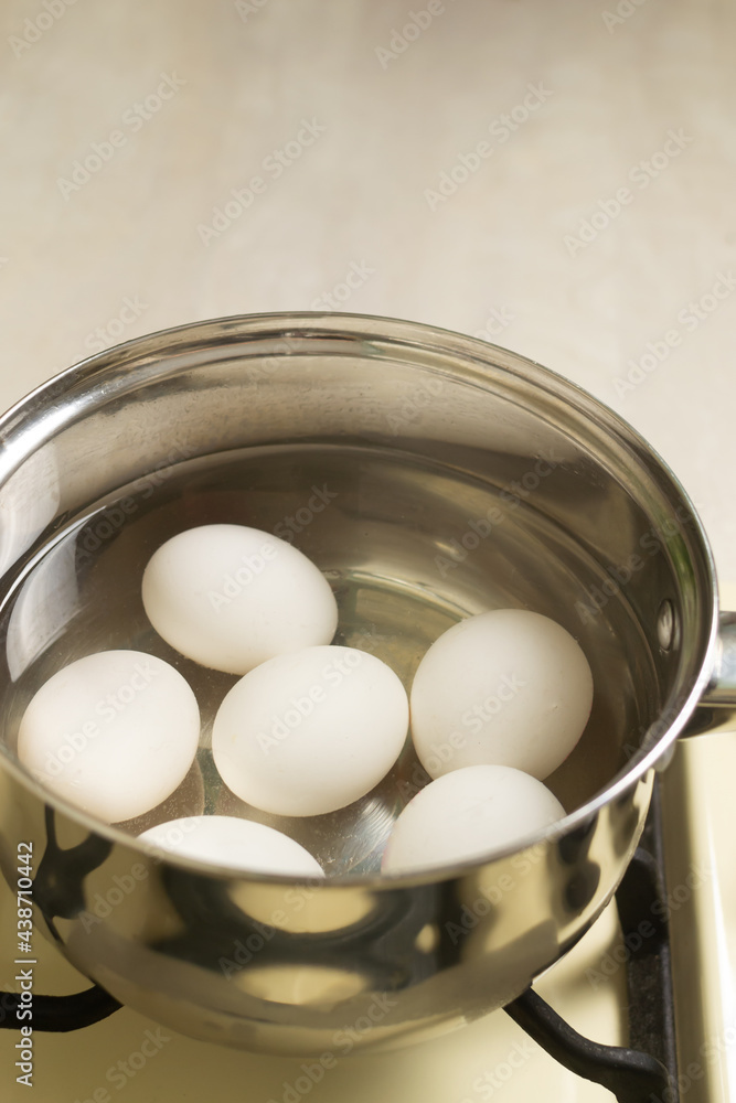 White chicken eggs are boiled in a ladle with wate on the stove White chicken eggs are boiled in a ladle with wate on the stove