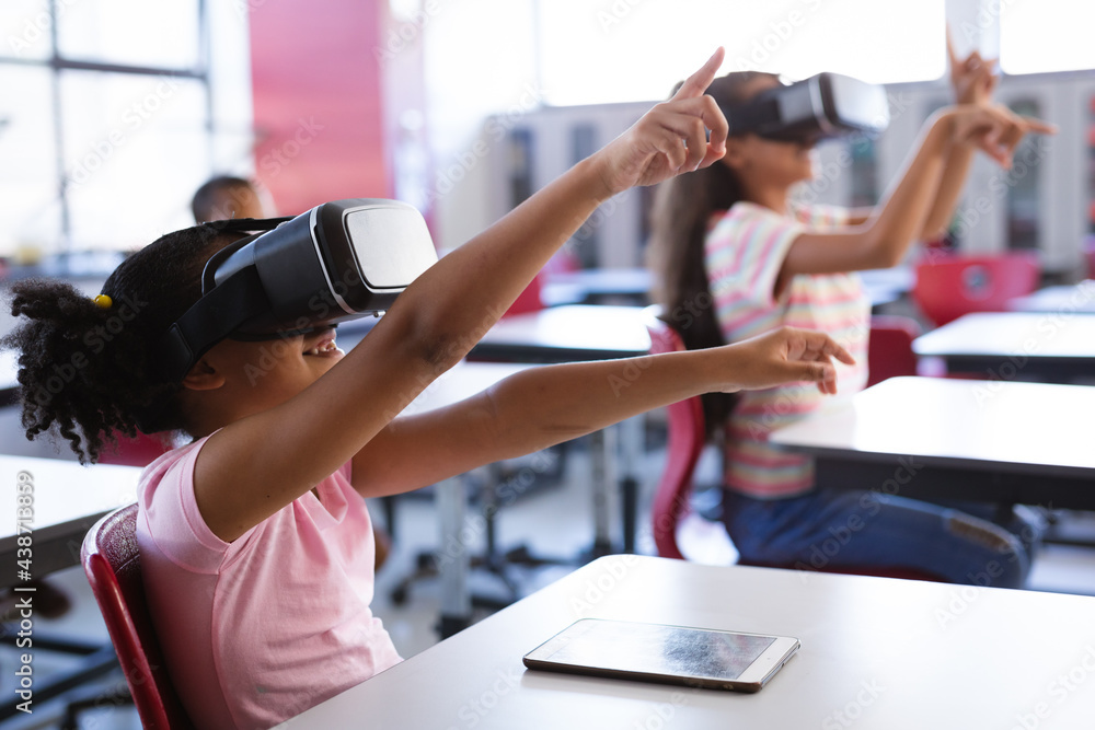 African american girl wearing vr headset gesturing while sitting on her desk in the class at school African american girl wearing vr headset gesturing while sitting on her desk in the class at school