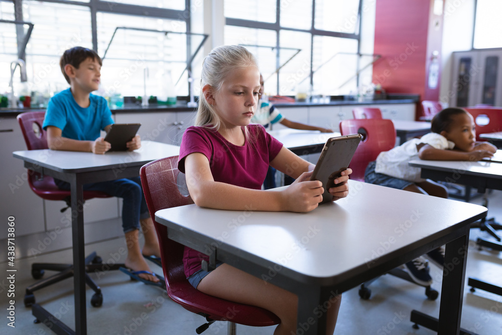 Caucasian girl using digital tablet while sitting on her desk in the class at school Caucasian girl using digital tablet while sitting on her desk in the class at school
