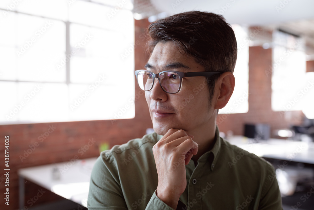 © wavebreak3 - Thoughtful asian businessman standing in office with hand under chin, looking away