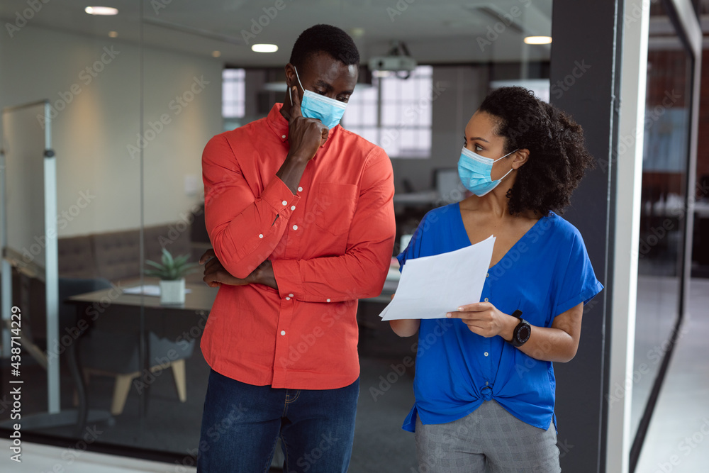 Diverse male and female colleague in face masks looking at paperwork and discussing in office Diverse male and female colleague in face masks looking at paperwork and discussing in office