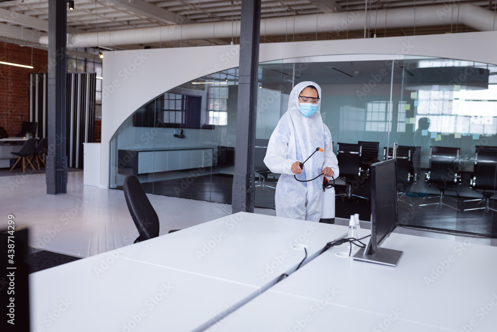 Cleaner wearing ppe suit, glasses and mask disinfecting office workspace