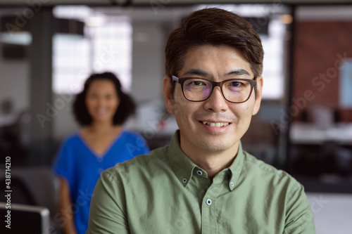 Portrait of smiling asian businessman standing in office with female colleague in background
