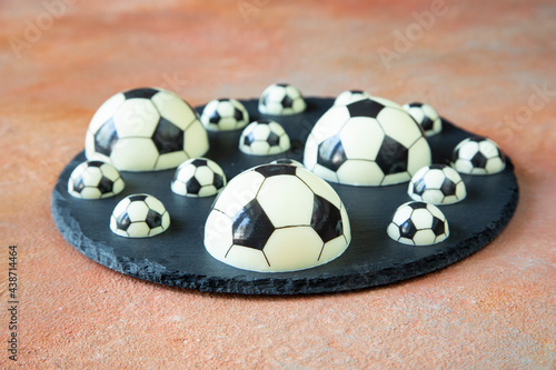Fototapeta Naklejka Na Ścianę i Meble -  A delicious dessert of chocolate football balls of different shapes on a black serving plate - a concept of sports photography for a football fan