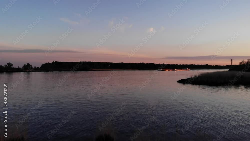Calm Riverside With Merchant Ship Navigating At Dusk Near Barendrecht, South Holland, Netherlands. - Low Aerial Shot Calm Riverside With Merchant Ship Navigating At Dusk Near Barendrecht, South Holland, Netherlands. - Low Aerial Shot