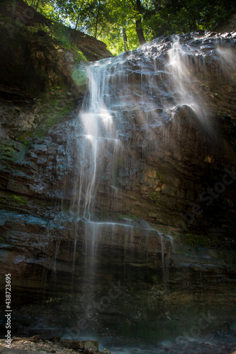 A waterfall flows down a rocky cliff in the middle of the forest  glistening in the sun poking through the trees in Hamilton  Ontario.