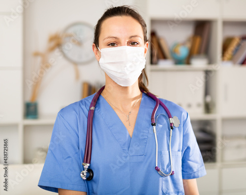 Portrait of a young female doctor in a protective mask, standing in the resident's office of a medical clinic. ..Close-up portrait