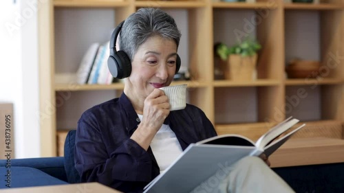 コーヒーを飲みながらヘッドホンをつけて本を読む日本人シニア女性