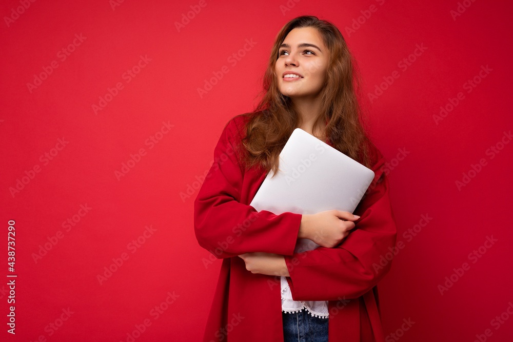 Photo of mysterious pretty young dark hair curly female student holding close netbook wearing red cardigan and white blouse looking to the side isolated over red background Photo of mysterious pretty young dark hair curly female student holding close netbook wearing red cardigan and white blouse looking to the side isolated over red background