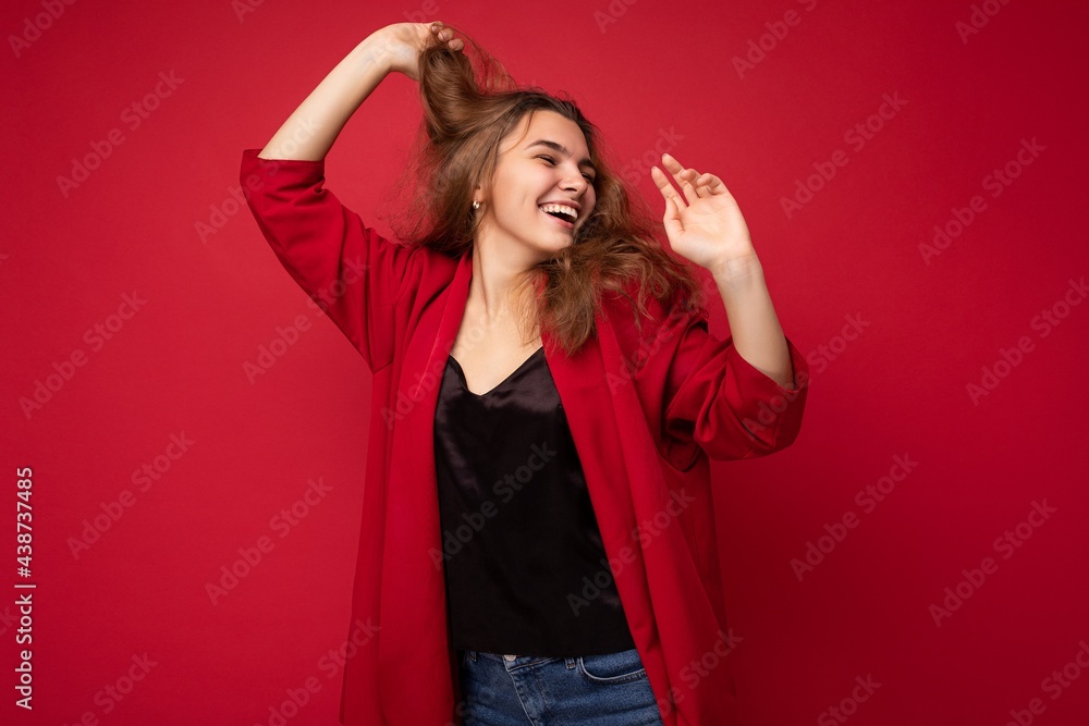 Naklejka premium Photo of young attractive caucasian hipster woman in trendy casual clothes. Sexy carefree female person posing isolated near red wall in studio. Positive model with natural makeup. Empty space