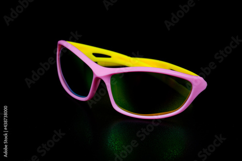 Children's glasses for cycling and sports. Made of pink plastic with yellow temples and UV-resistant lenses. Photographed on a black background.