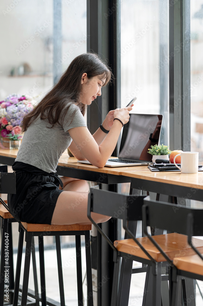 Young asian woman using smartphone and computer while sitting at co-workspace.