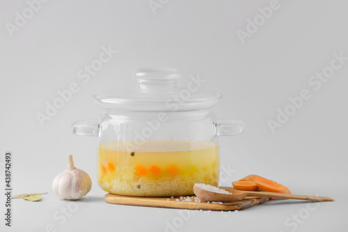 Stylish cooking pot with hot soup and ingredients on light background