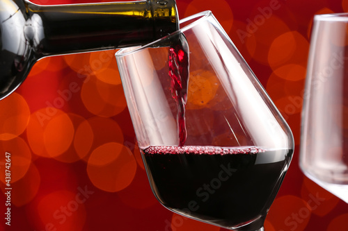 Pouring of tasty red wine into glass on blurred background, closeup