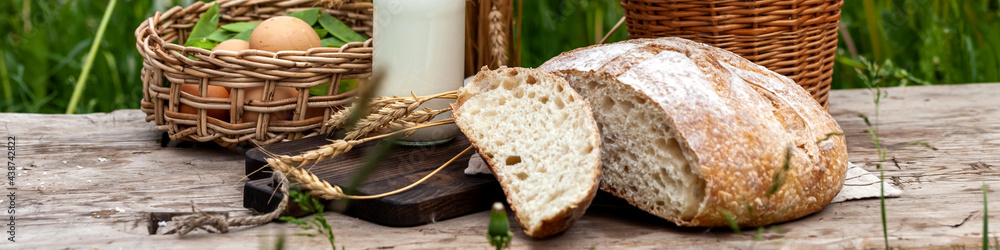 Concept of natural organic products from the local farm. Homemade bread, fresh milk, eggs. Wooden background, outdoors. Close up, copy space for text. Banner