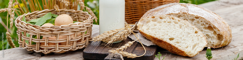 Concept of natural organic products from the local farm. Homemade bread, fresh milk, eggs. Wooden background, outdoors. Close up, copy space for text. Banner