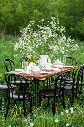 Elegant wedding dinner table decorated with white dishes, flowers in glass vases. Festive atmosphere, luxury party. Sunset, bright summer evening. Close up, details