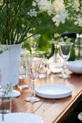 Elegant wedding dinner table decorated with white dishes, flowers in glass vases. Festive atmosphere, luxury party. Sunset, bright summer evening. Close up, details © ArtSys