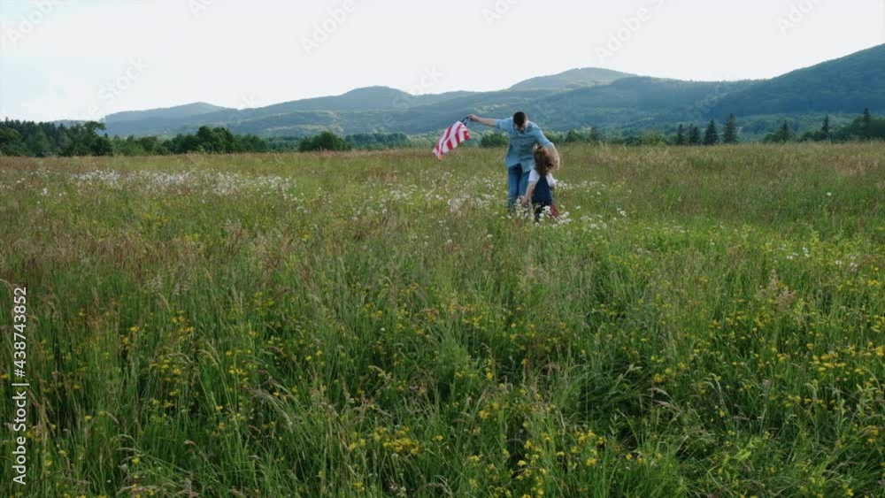 Happy little daughter and joyful dad holds flag of United States runs enjoying amazing summer nature. Celebrating independence day of USA on 4th of July with family. American patriotic holiday concept Happy little daughter and joyful dad holds flag of United States runs enjoying amazing summer nature. Celebrating independence day of USA on 4th of July with family. American patriotic holiday concept