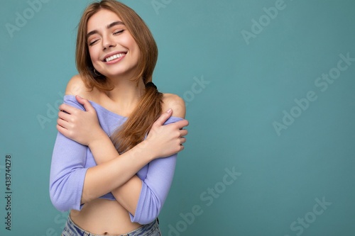 Photo of young happy pretty dark blond woman with sincere emotions isolated on background wall with copy space wearing casual blue crop top. Positive concept