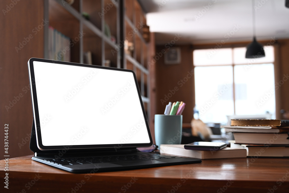 Close up view of mock up computer tablet with blank screen and books on wooden desk in library. Close up view of mock up computer tablet with blank screen and books on wooden desk in library.