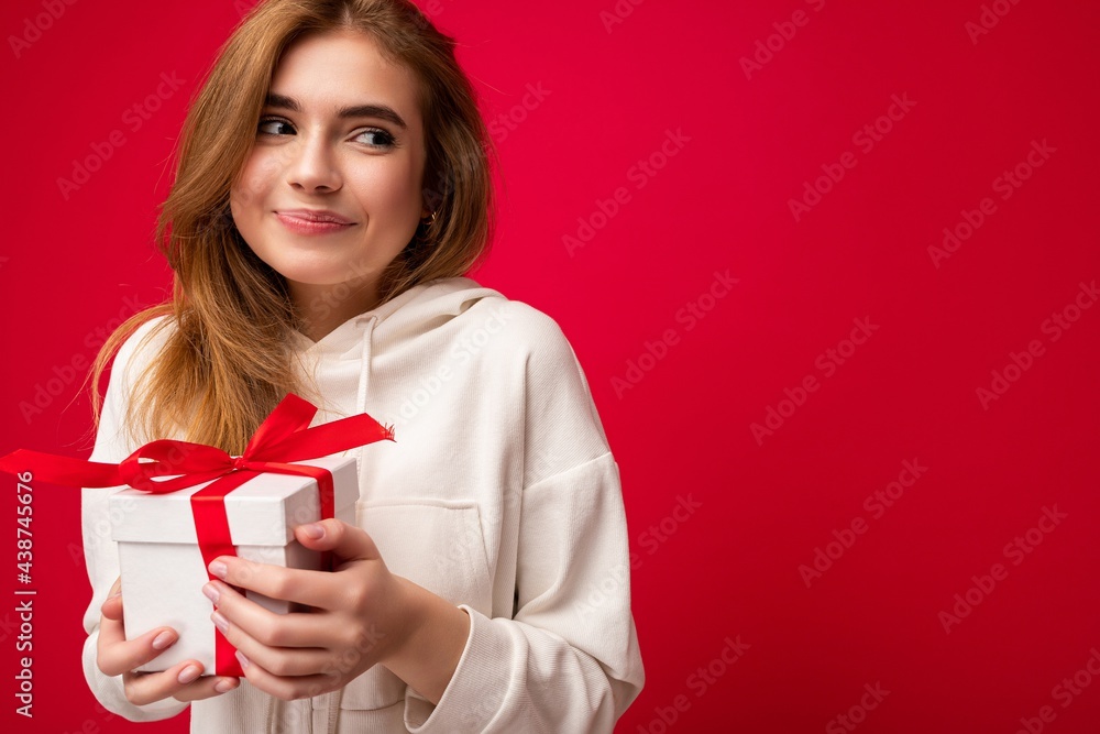 Shot of attractive positive smiling young blonde woman isolated over colourful background wall wearing everyday trendy outfit holding gift box and looking to the side Shot of attractive positive smiling young blonde woman isolated over colourful background wall wearing everyday trendy outfit holding gift box and looking to the side