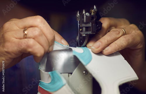 Shoe factory worker making shoes. Woman using industrial sewing machine to stitch detail for new leather sneakers, needle and hands holding material in closeup. Footwear manufacturing industry concept
