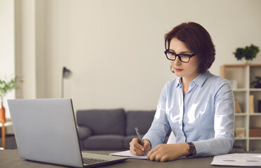 Distance learning at home. Concentrated woman watching online workshop or attending continuing education webinar on laptop computer. Focused employee with attention to detail studying new information