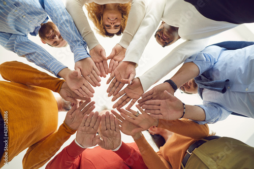 Many human hands joint together. Team of positive young and senior people join hands in circle. Diverse community, teamwork, help and making agreement concepts. Low angle shot, bottom view, from below