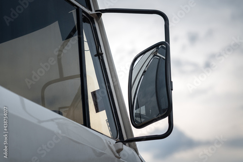 Side mirror of the heavy truck or cargo trailer, vehicle part. Transportation and logistic industrial equipment object. Close-up and selective focus photo.