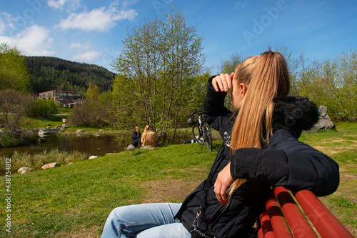 Young woman sitting on a bench in a beautiful park looking at other people. photo