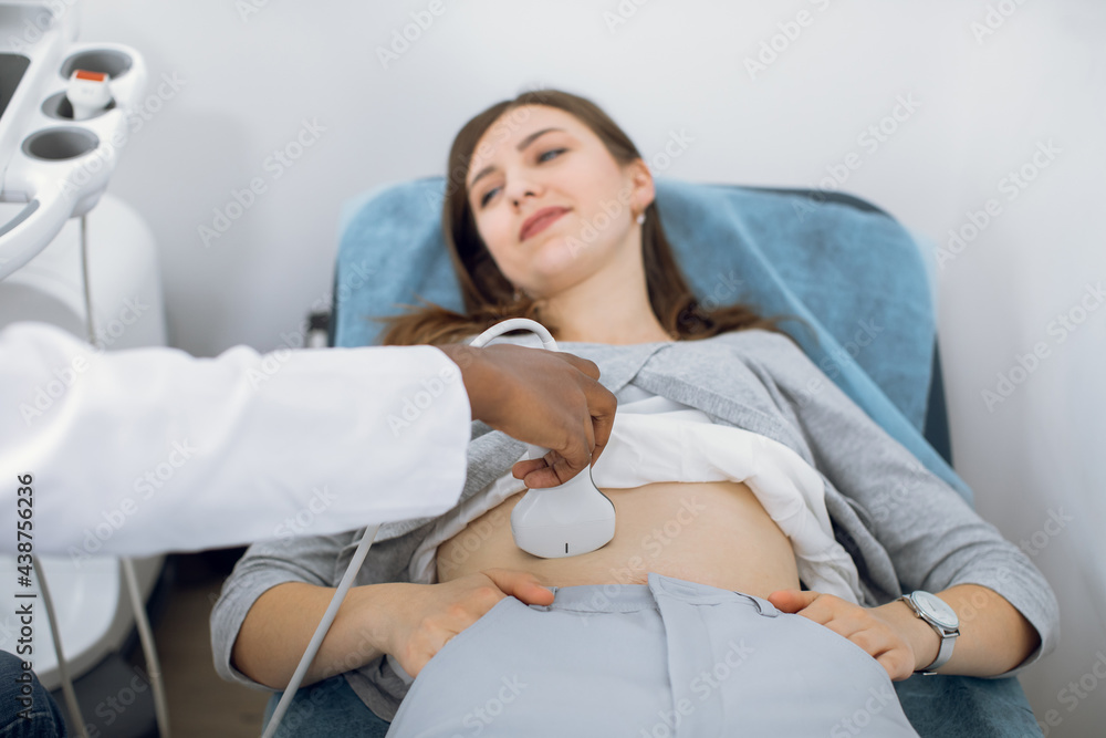 ultrasound scanner device in the hand of a professional African American doctor examining young woman patient, doing abdominal ultrasound scanning sonography ultrasound scanner device in the hand of a professional African American doctor examining young woman patient, doing abdominal ultrasound scanning sonography