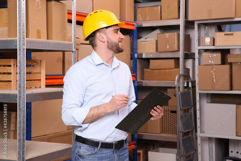 Young man with clipboard near rack of cardboard boxes at warehouse Young man with clipboard near rack of cardboard boxes at warehouse