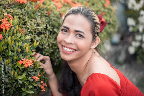 A happy and upbeat transgender woman inspects some santan flowers. Of Southeast Asian descent. Garden setting. photo