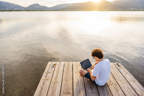 Nerd guy spending time outdoor programming at sunset writing code using laptop. New job opportunity at modern times to work everywhere using notebook and wifi 5g or 4g internet connection technology photo