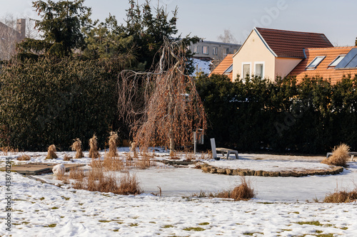 Vaclav Havel Park, garden trees and small pond under snow at sunny day, building with red tile roof, Litomerice, Czech Republic photo