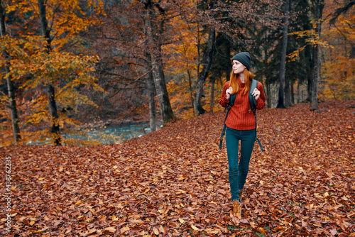 travel tourism and a young woman with a backpack walks in the park in nature landscape tall trees fallen leaves river